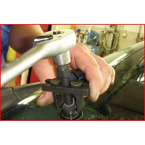 Eine Hand bedient eine Ratsche, die ein Werkzeug auf einer Autoscheibe betätigt. Das Werkzeug ist auf das Glas aufgesetzt.